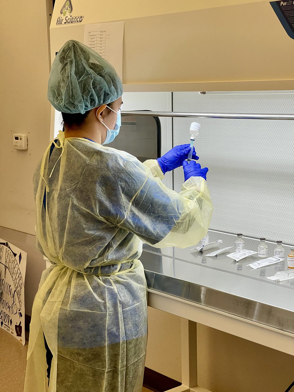 Woman in protective scrubs holds vial of medicine