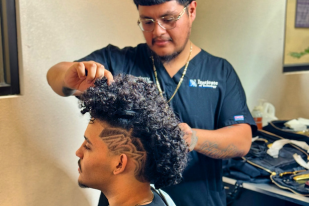 Institute of Technology Barbering student practicing professional haircutting techniques in a hands-on training salon.